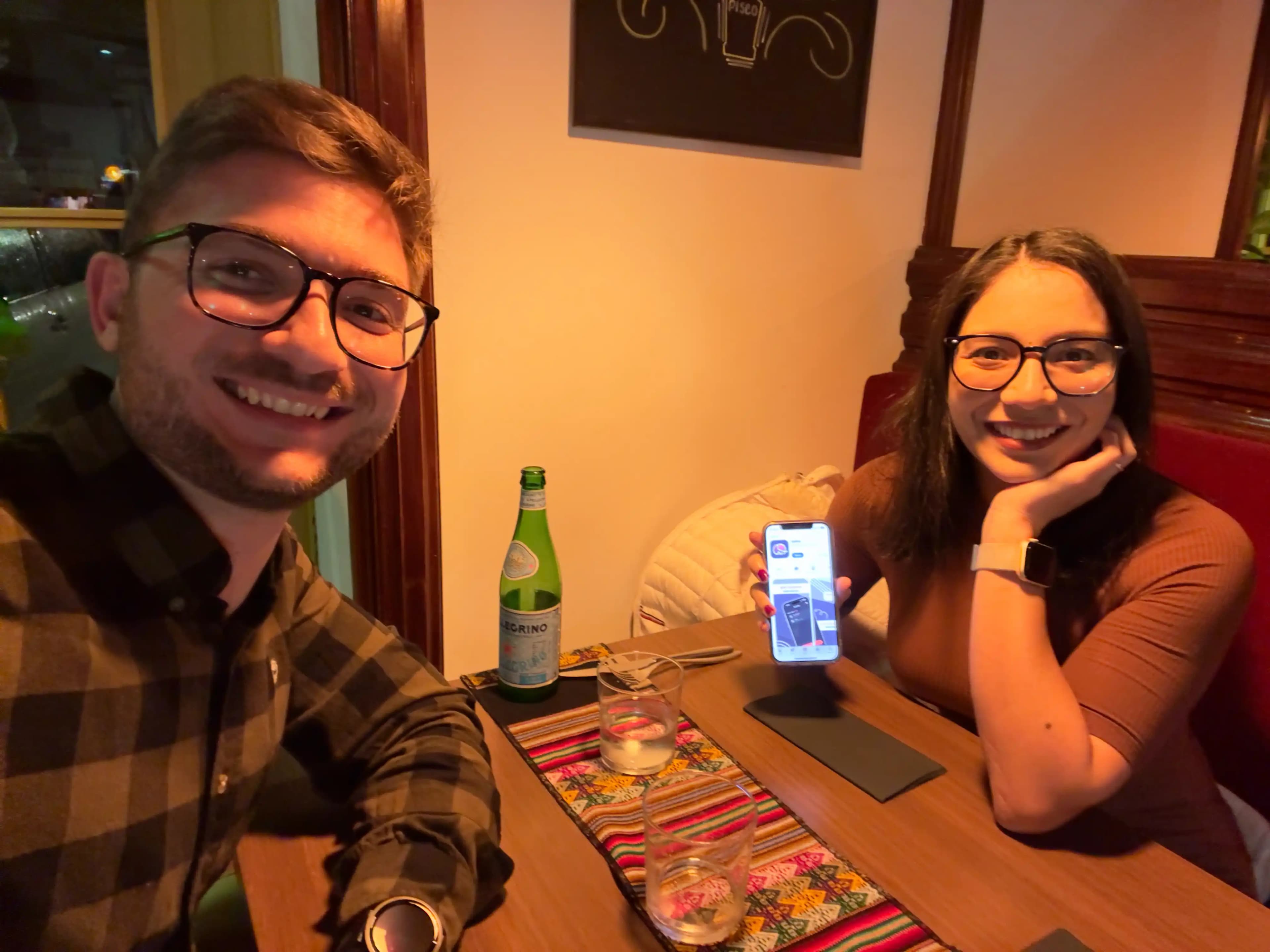 Maria and Maurizio at dinner on Splital's launch day, with Maria holding her iPhone showing Splital on the App Store.